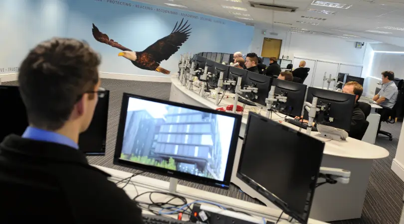 Control room with staff monitoring vehicle tracking systems on multiple computer screens in a 24/7 UK-based tracking centre.